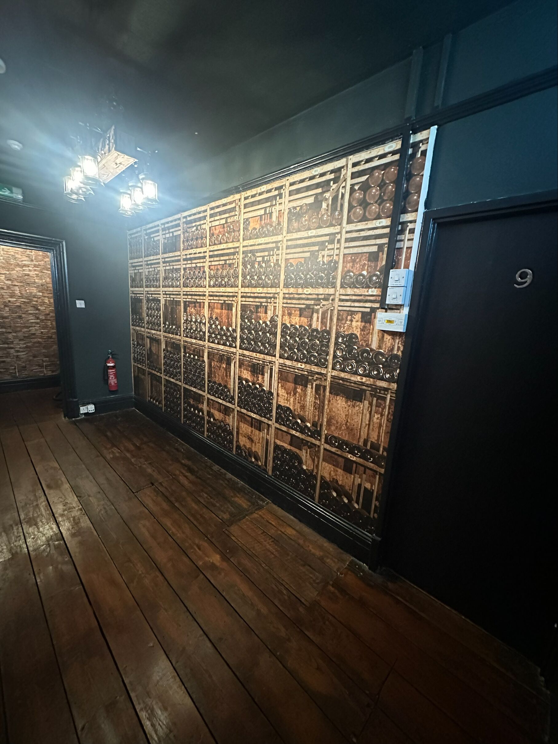 A room with wooden flooring, a wall-mounted rack of wine glasses, and a black door with a number '9' on it.
