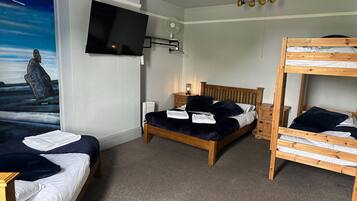 A room with a bunk bed, a single bed, a flat-screen TV, a radiator, and a wall mural.