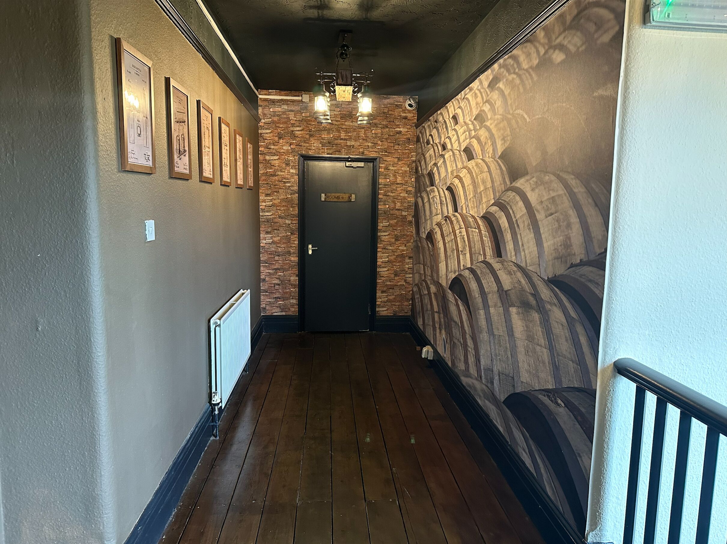 Un pasillo con suelo de madera, pared de ladrillo y una puerta con la inscripción "ROOM 6".