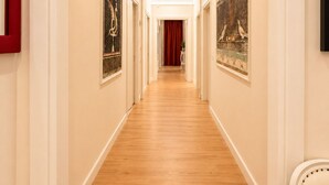 A hallway with wooden flooring, framed artwork on the walls, and a red curtain at the end. - Roma in una Stanza GuestHouse (Rome)