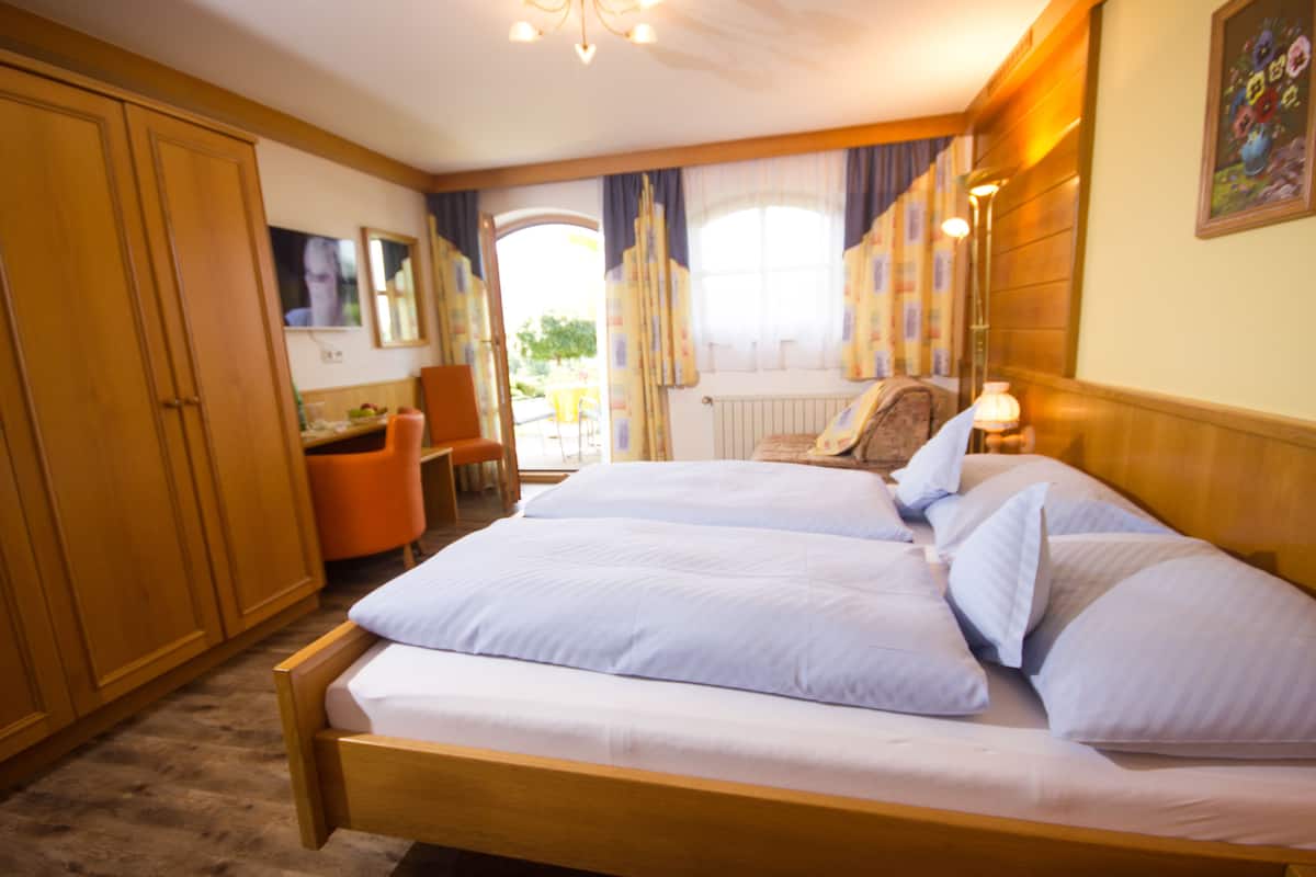 A bedroom with a large bed, wooden wardrobe, and a desk with a chair.