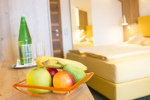 Uma tigela de frutas sobre uma mesa de madeira, com uma cama e um abajur ao fundo.