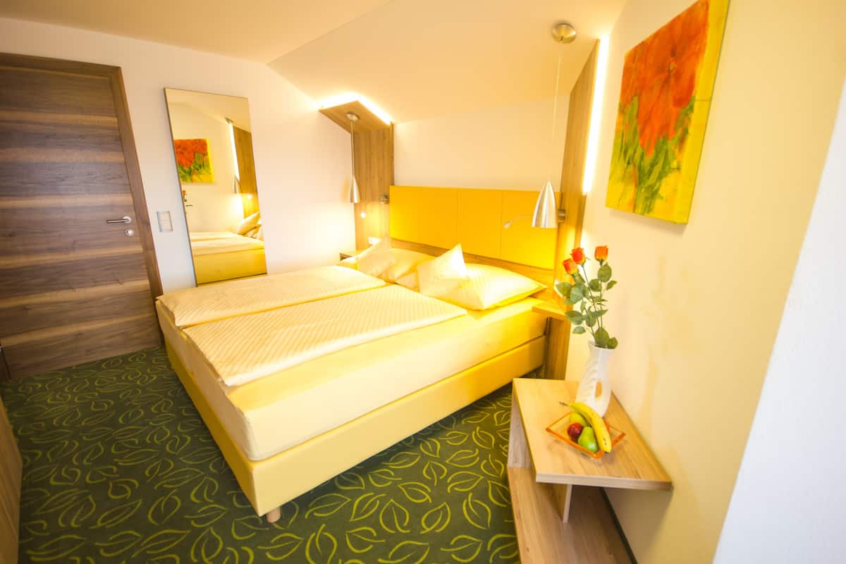 A hotel room with a bed, a bedside table with a fruit bowl, a mirror, and a painting on the wall.