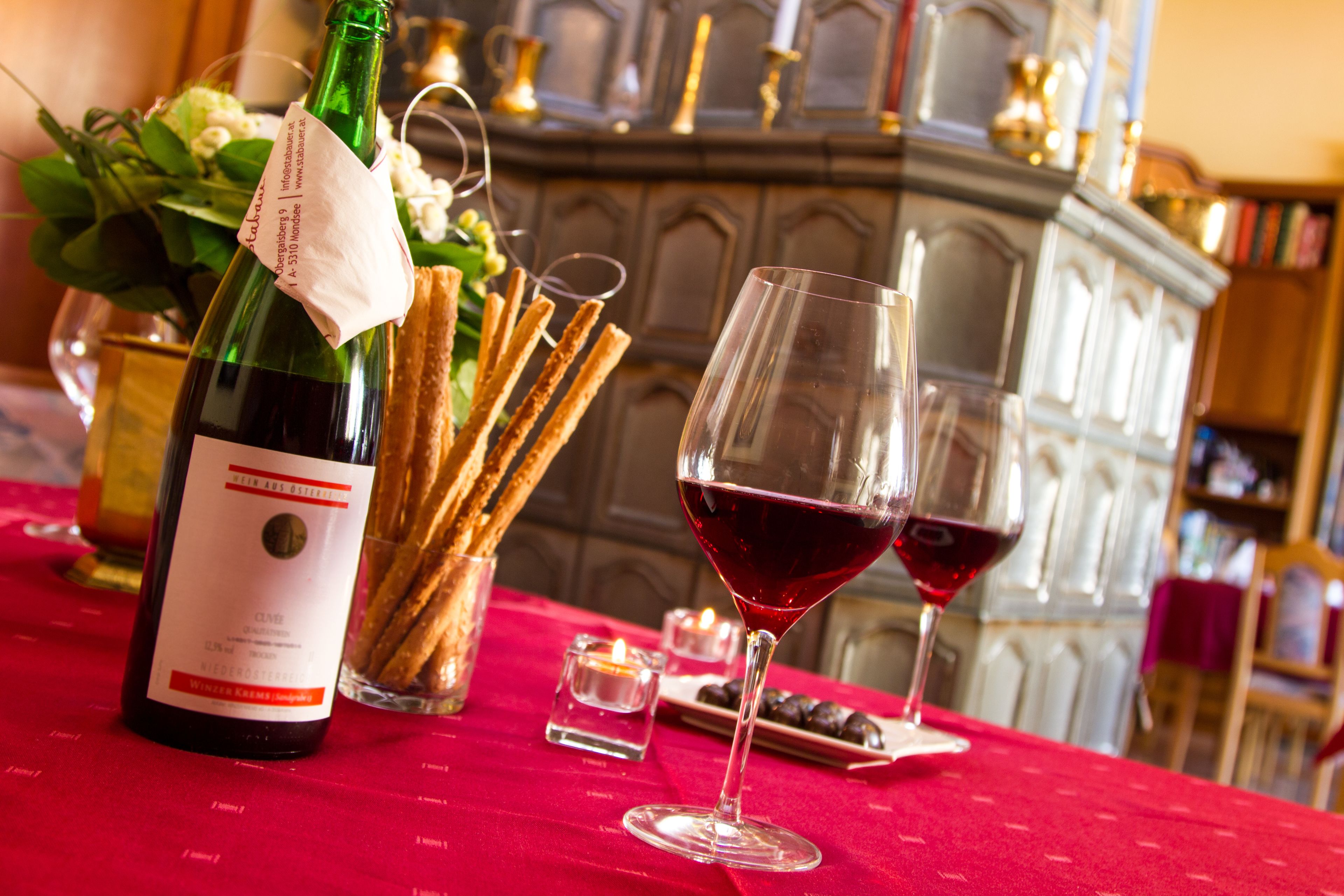 Une table avec une bouteille de vin, des verres, des gressins et des bougies.