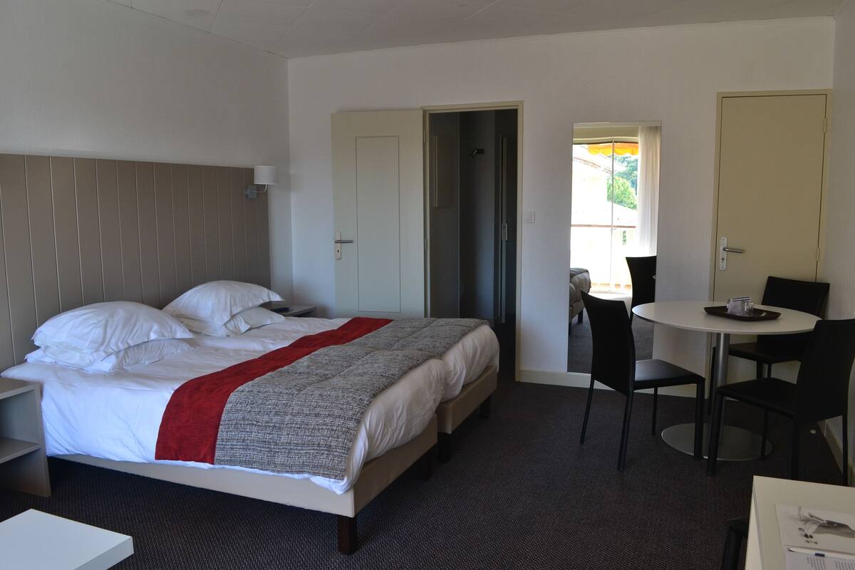 A hotel room with a bed, a desk, a chair, and a door leading to a balcony.