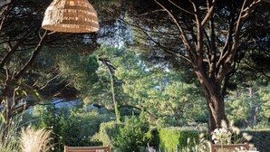 An outdoor dining area with wicker furniture, hanging rattan light fixtures, and a view of a lush garden. - Hôtel Maison Chiberta (Anglet)