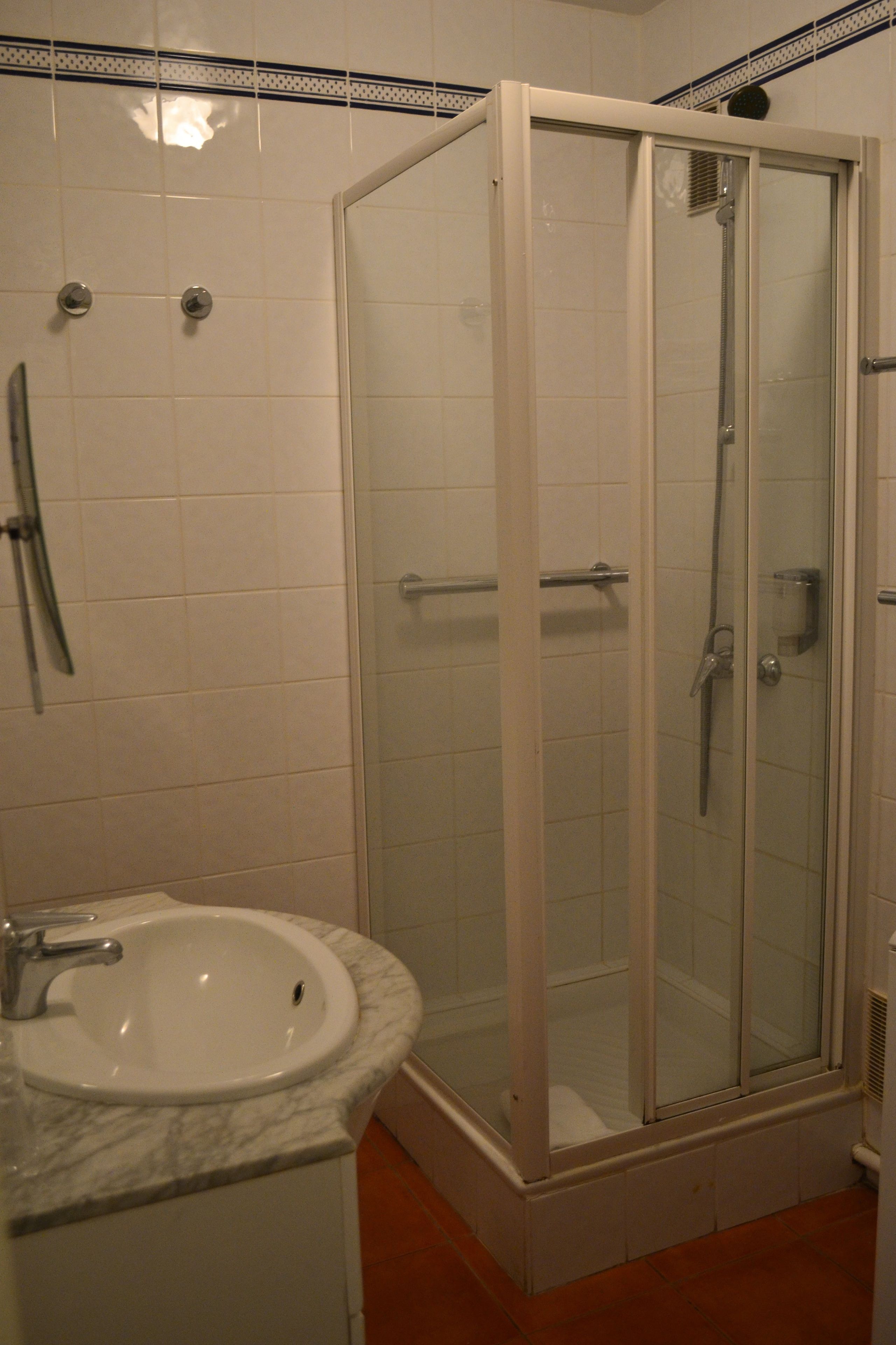 A bathroom with a glass-enclosed shower, a sink with a marble countertop, and tiled walls.