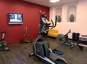 A gym with cardio machines, a TV, and a yellow chair. - Hôtel Maison Chiberta (Anglet)