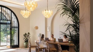 A reception area with a wooden reception desk, wicker chairs, and a large potted plant. - Hôtel Maison Chiberta (Anglet)