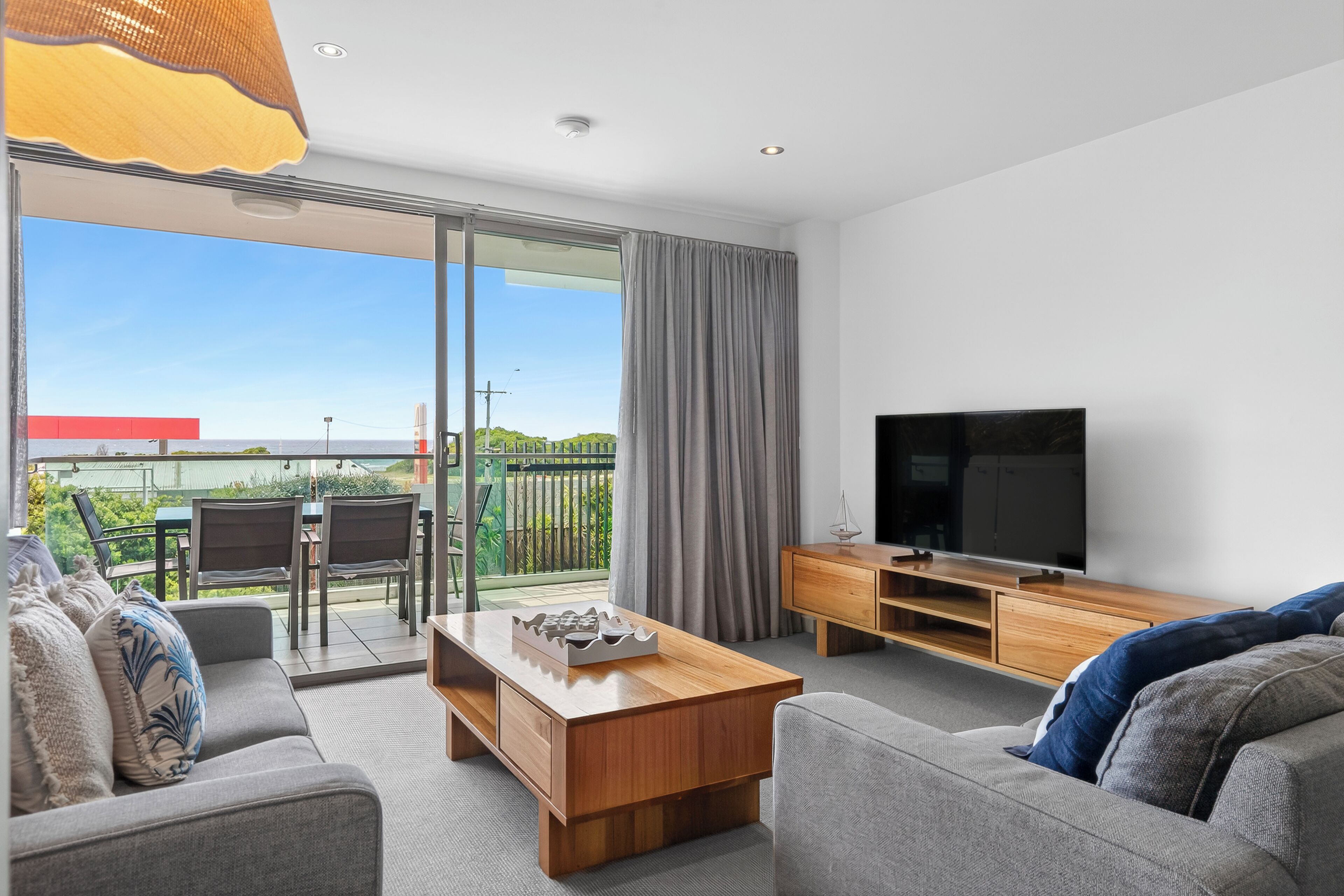 Ein modernes Wohnzimmer mit Sofa, Couchtisch, TV-Schrank und einem Balkon mit Gartenmöbeln.