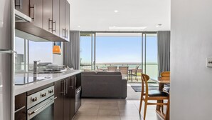 Een moderne keuken met een inbouwoven, een zithoek met een tafel en stoelen, en een groot raam met uitzicht op zee.
