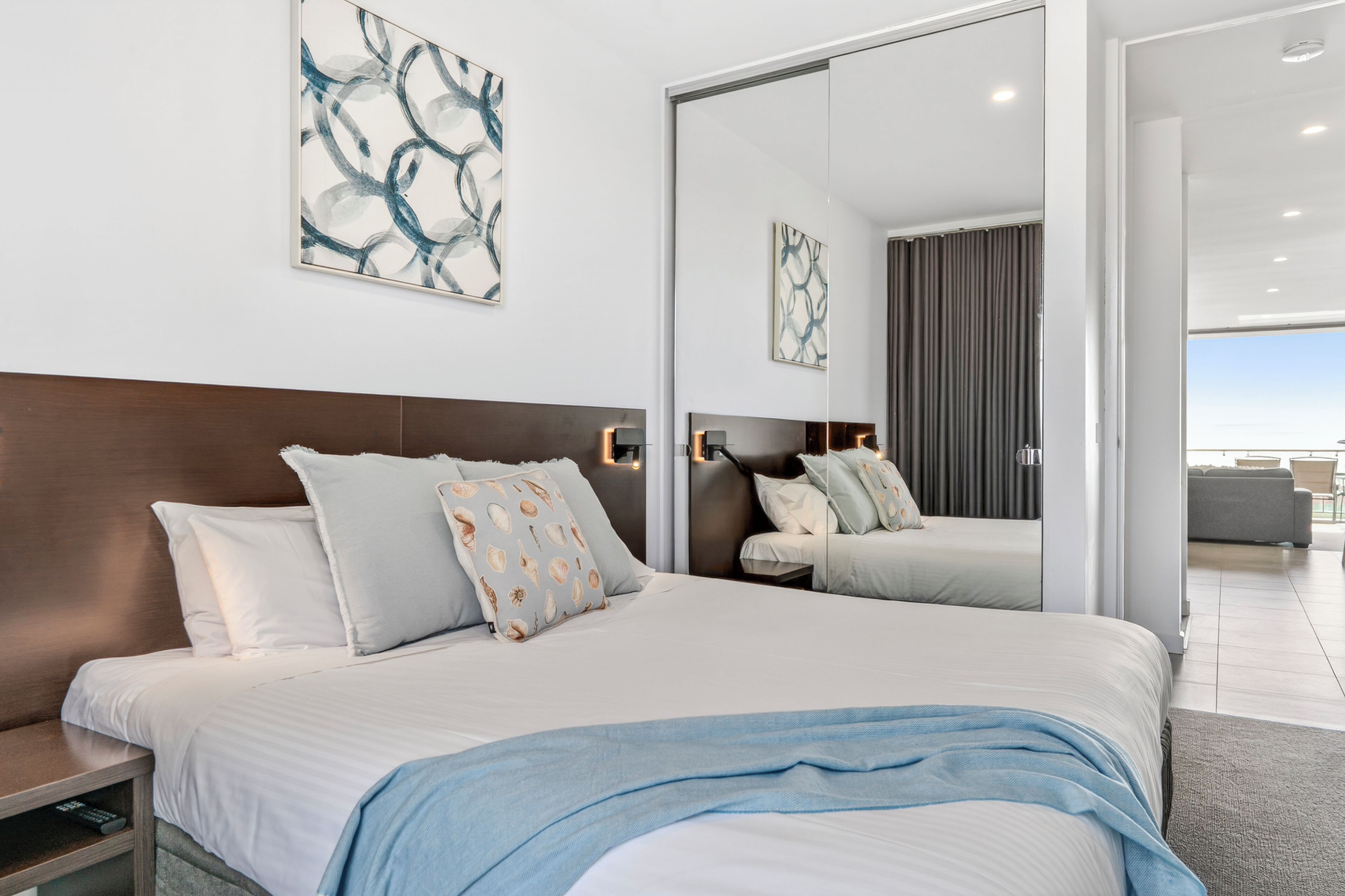 A modern hotel room with a large bed, a nightstand, a mirror, and abstract wall art.