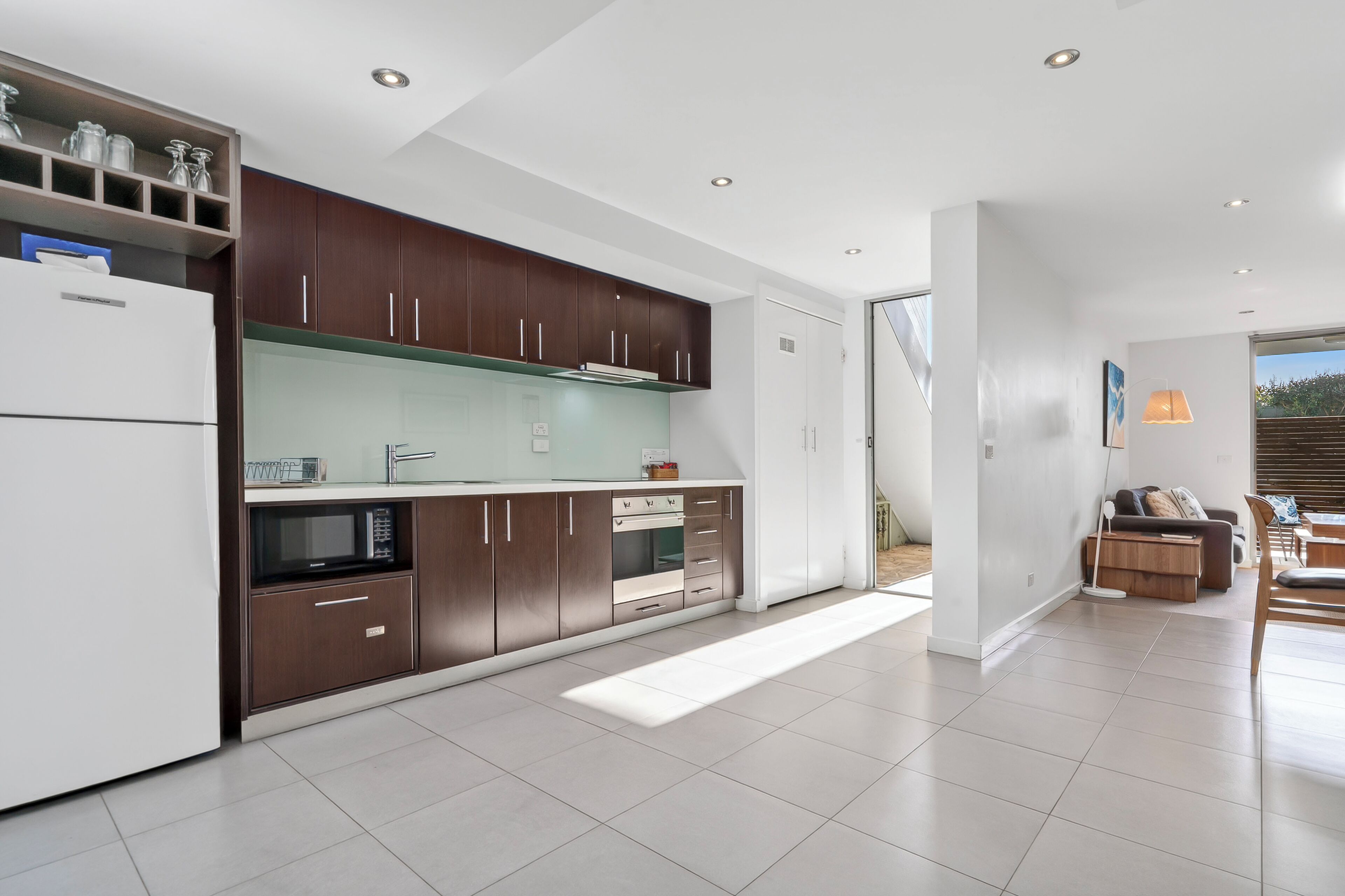 A modern kitchen with dark wood cabinets, a white refrigerator, and a built-in oven.