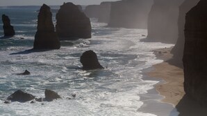 Een kustlandschap met grote rotsformaties en een zandstrand.