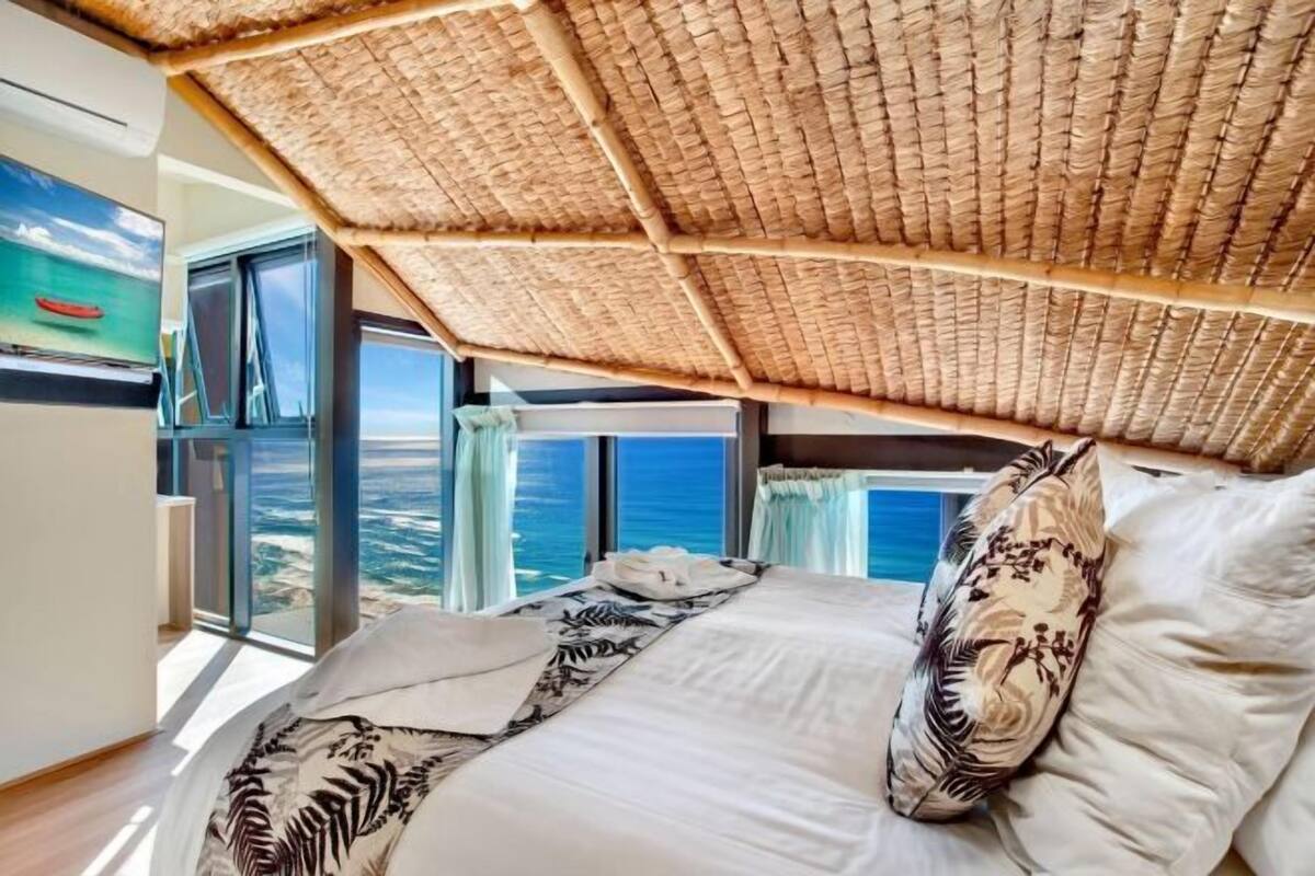 Quarto com cama grande, vista para o oceano e teto de palha.