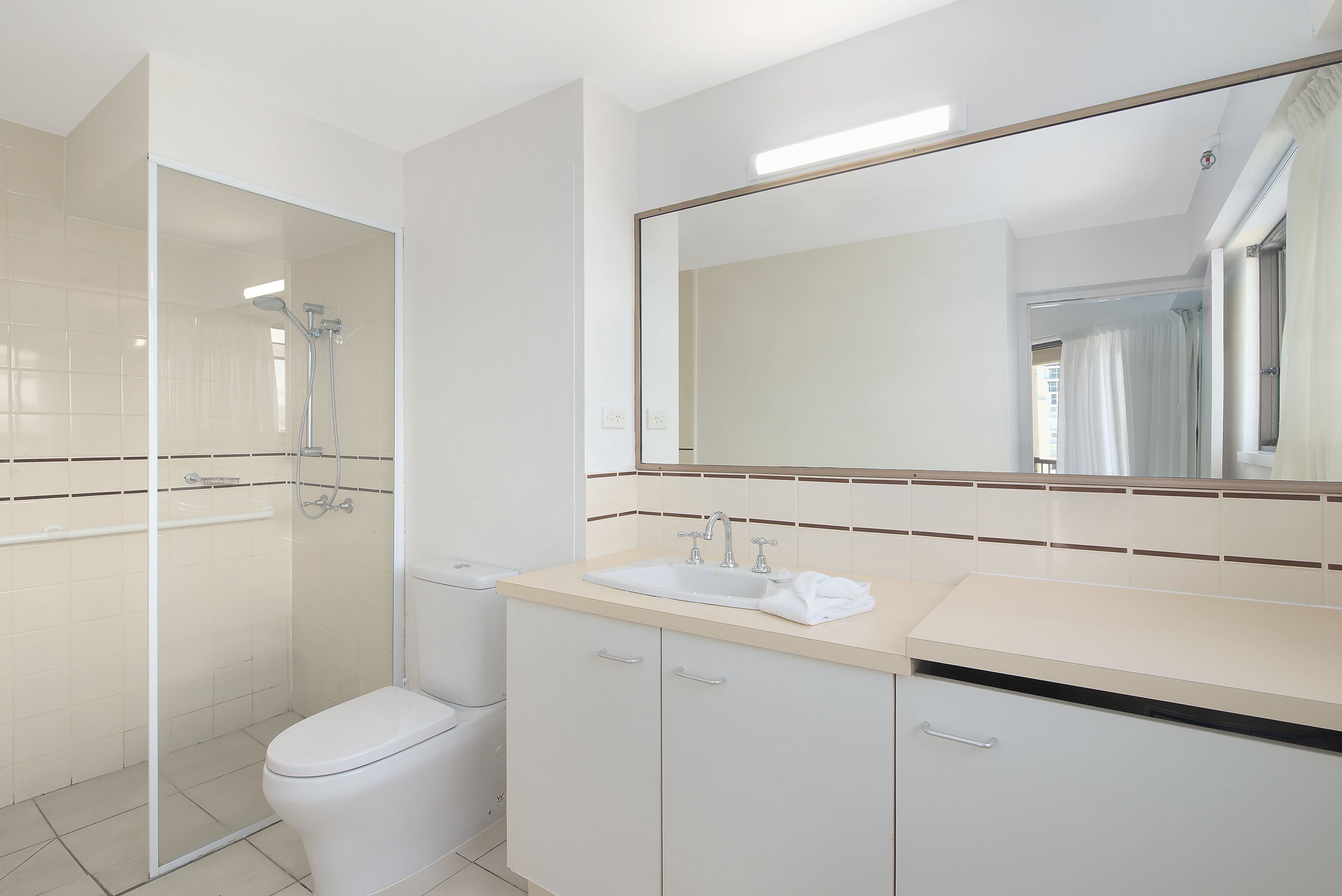 A modern bathroom with a glass-enclosed shower, a toilet, a sink with a towel, and a large mirror.