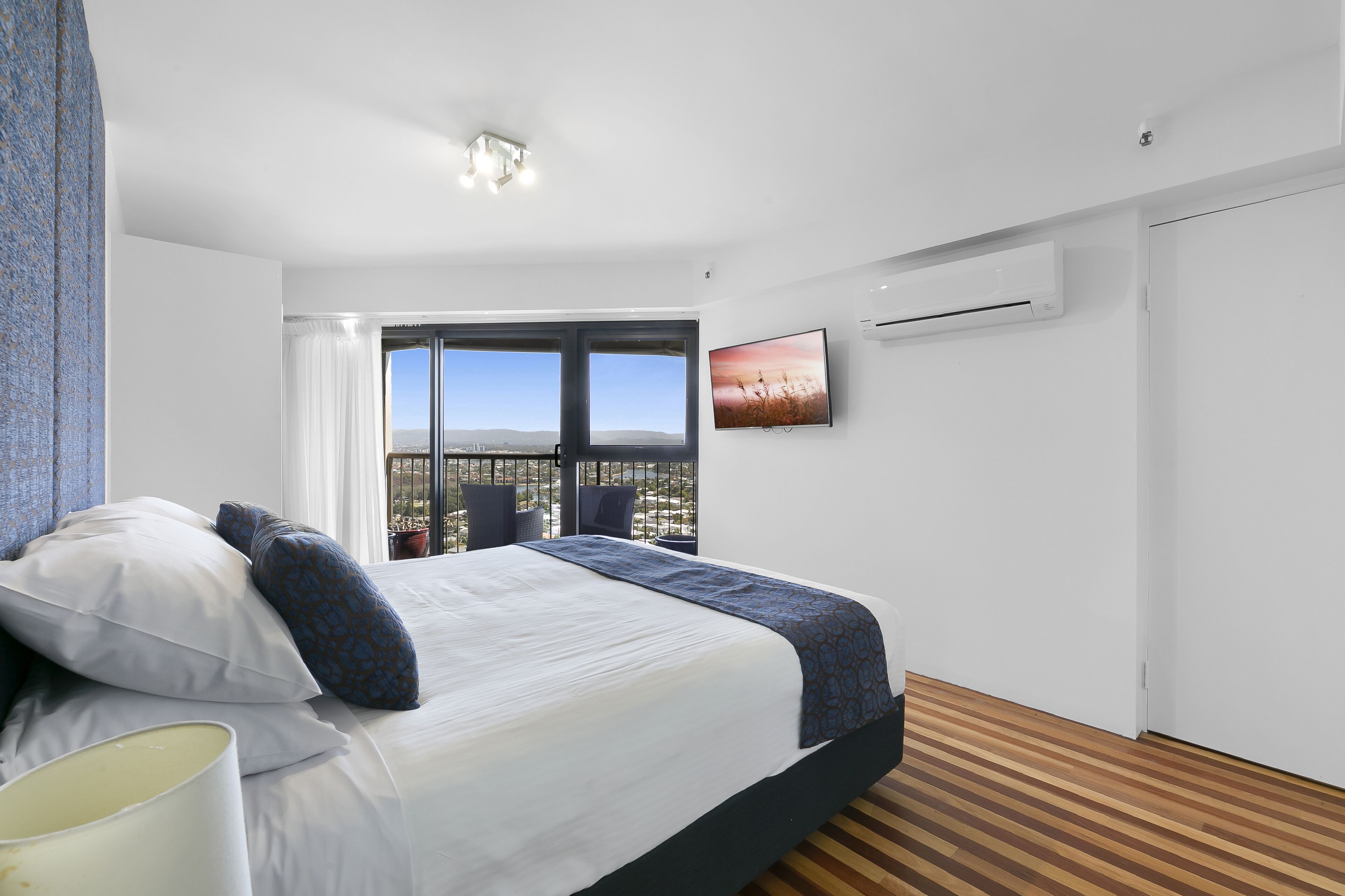 A modern hotel room with a large bed, a view of the countryside, and a balcony with chairs.
