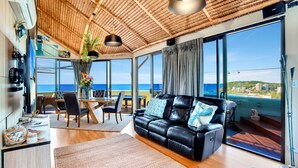 Una sala de estar moderna con sofá de cuero, comedor y grandes ventanales con vistas al mar.