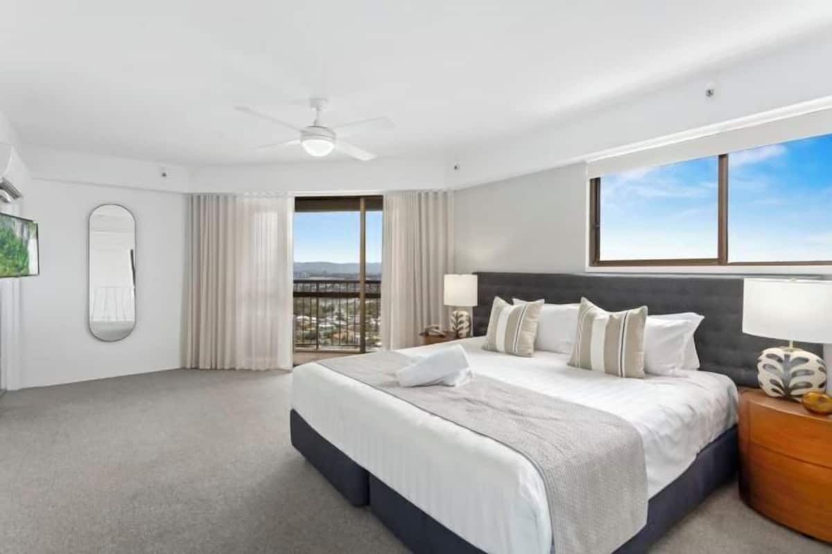 Quarto de hotel moderno com uma cama grande, ventoinha no teto, vista para a cidade e varanda.