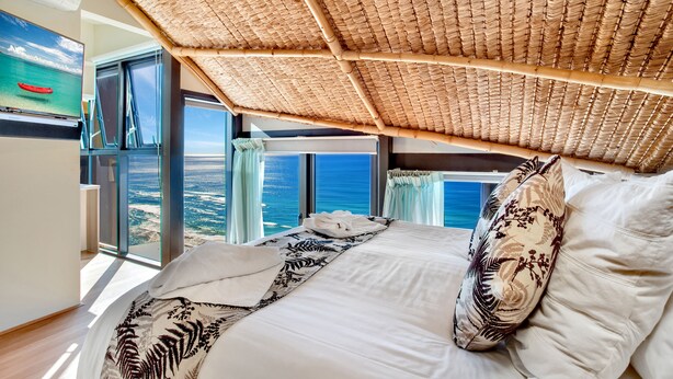 Un dormitorio con una cama grande, vista al océano y techo de paja.