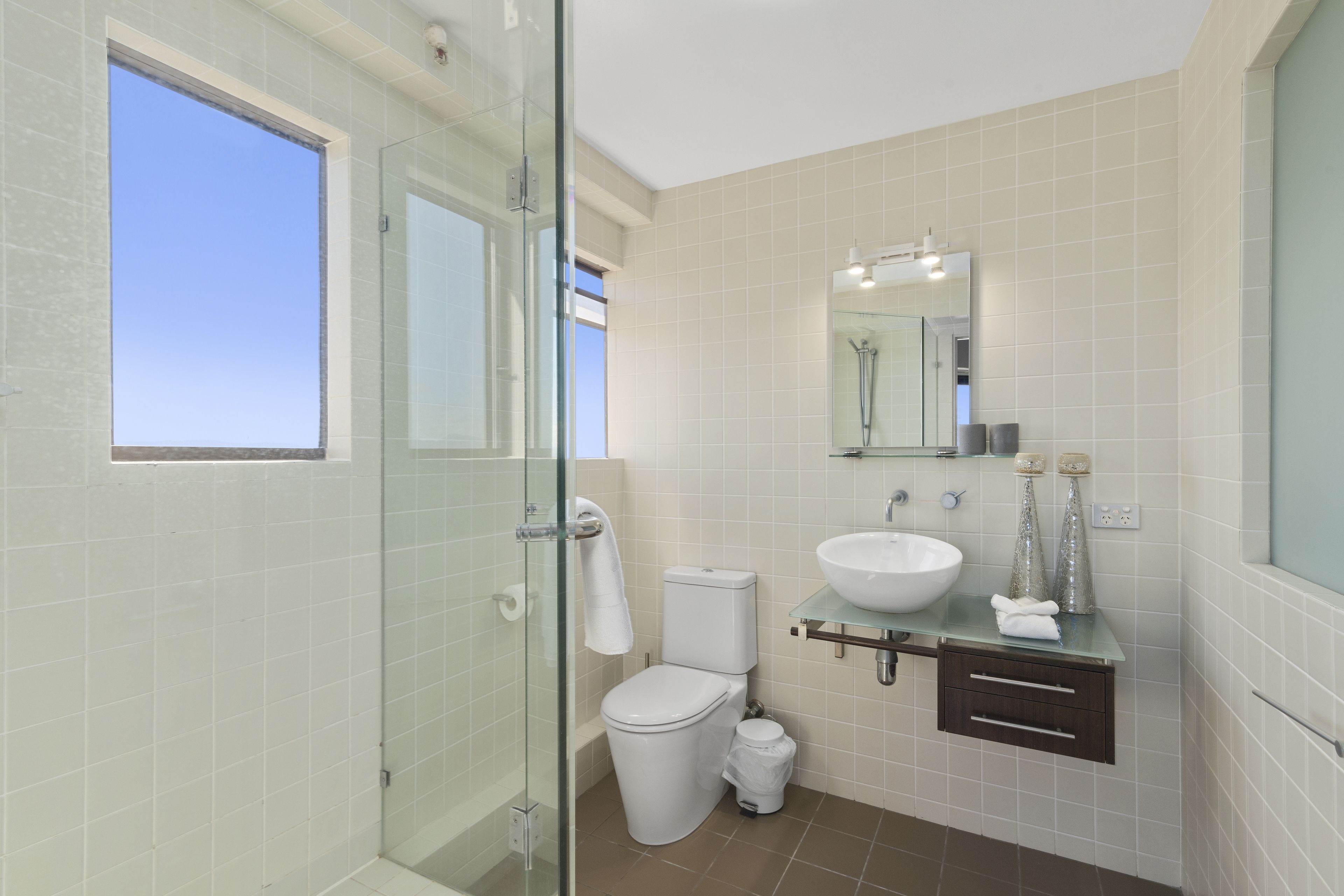 Ein modernes Badezimmer mit Duschkabine aus Glas, einer weißen Toilette, einem Waschbecken und einem Spiegel darüber.