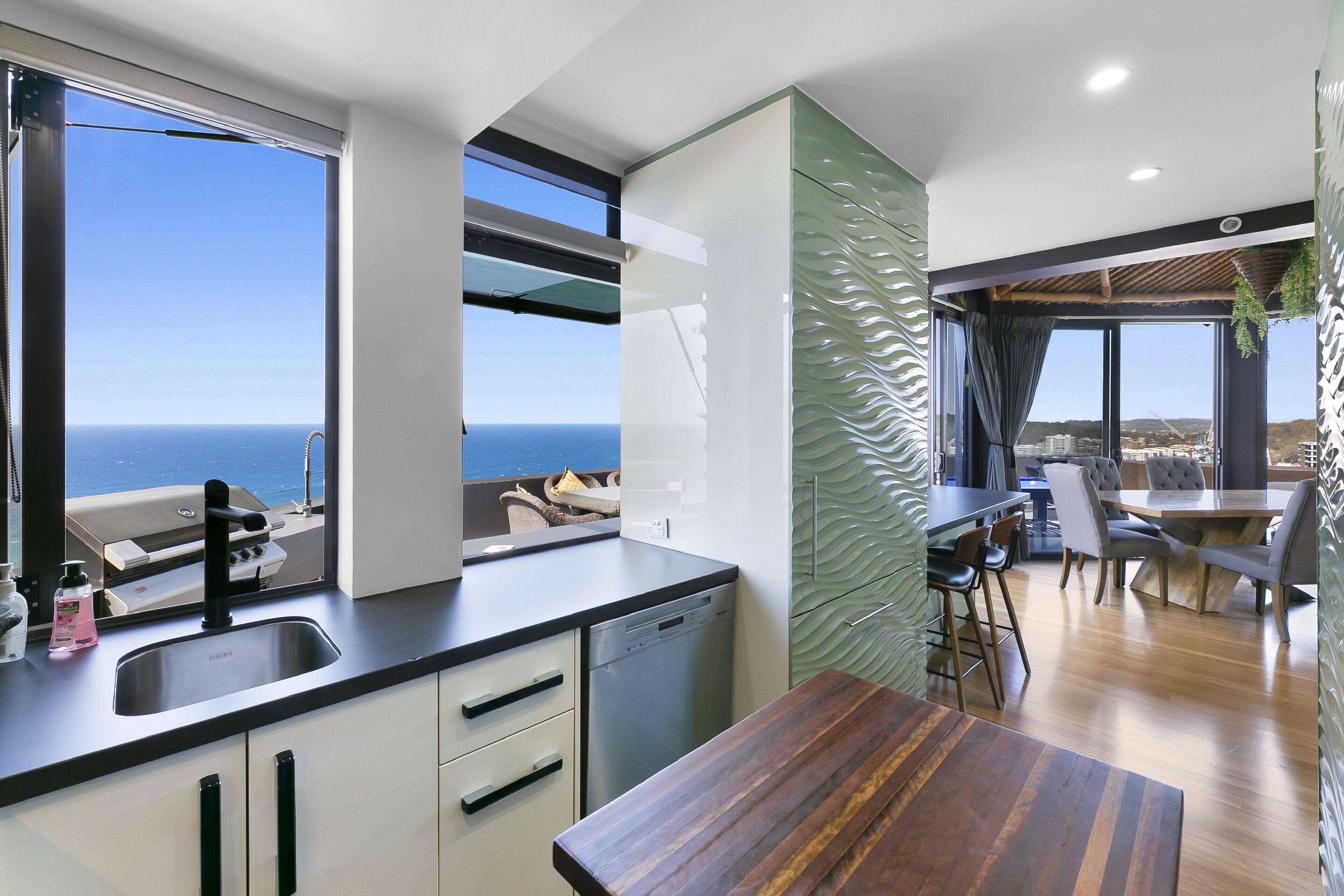 Una cocina moderna con vista al mar, un comedor con mesa de madera y una barra también con vista al mar.