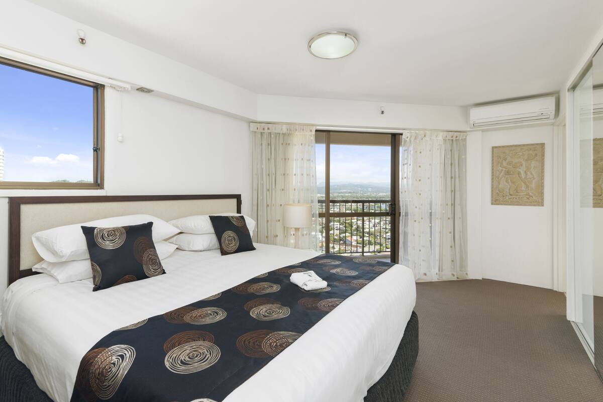 Quarto de hotel com uma cama grande, vista da cidade por uma varanda e uma janela com cortinas.