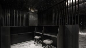Ein modernes, minimalistisches Zimmer mit dunkler Farbgestaltung, Marmorboden, zwei Hocker und einem einzigartigen Deckengestaltung mit Sternenmuster.