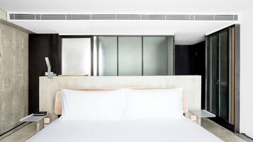 A modern hotel room with a large bed, a bedside table, a nightstand, and a large window with blinds.