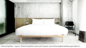 Ein modernes Schlafzimmer mit einem großen Bett, einem Holzkopfteil, einem schwarzen Stuhl und einer Wand mit Betonoptik.