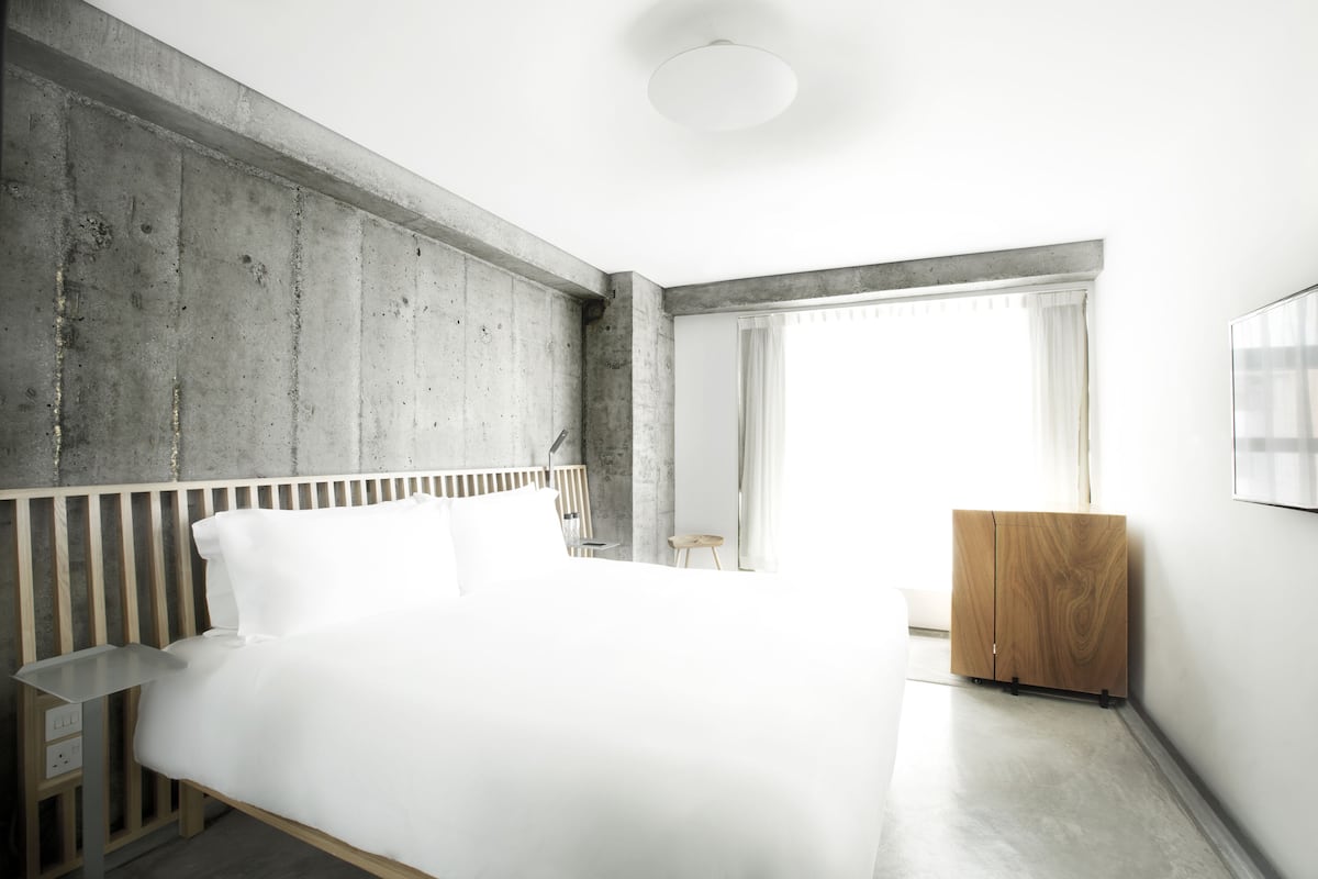 A modern bedroom with a large bed, a wooden nightstand, a small stool, and a wooden cabinet.