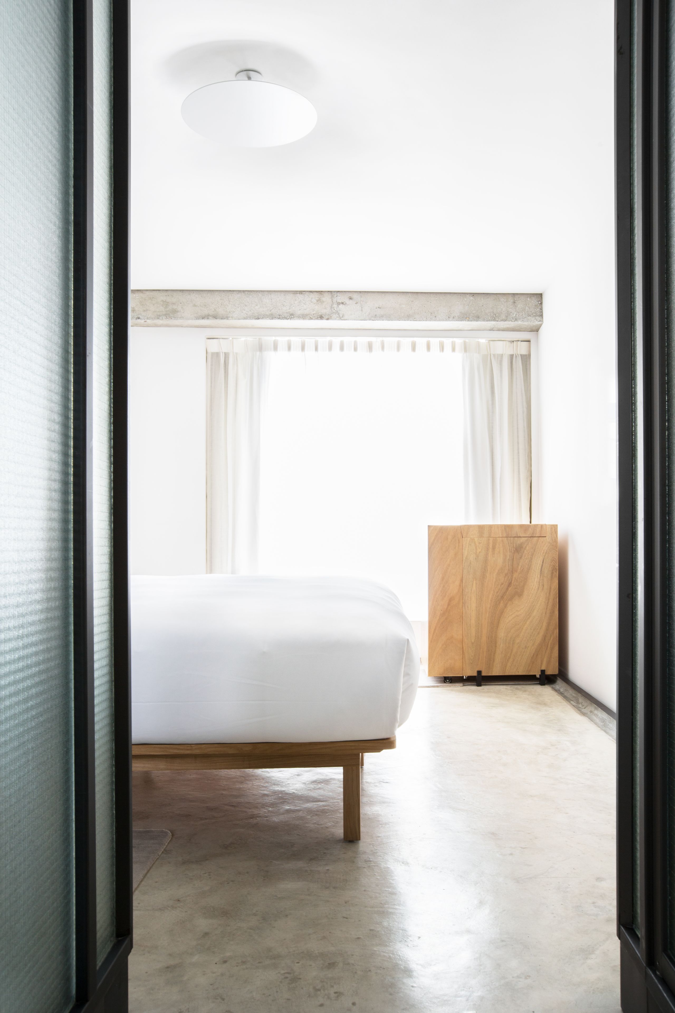 A bedroom with a bed, a wooden sideboard, and a window with curtains.