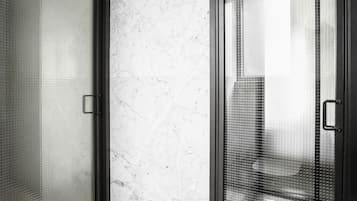 Une salle de bain moderne avec une douche à l’italienne en verre, des murs en marbre et une bouche d’aération visible au plafond.
