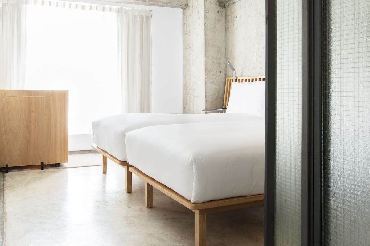 A modern hotel room with two beds, a wooden dresser, and a large window with curtains.