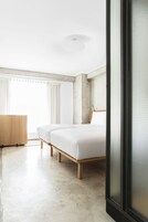 Una habitación de hotel moderna con dos camas, un aparador de madera y un ventanal con cortinas.