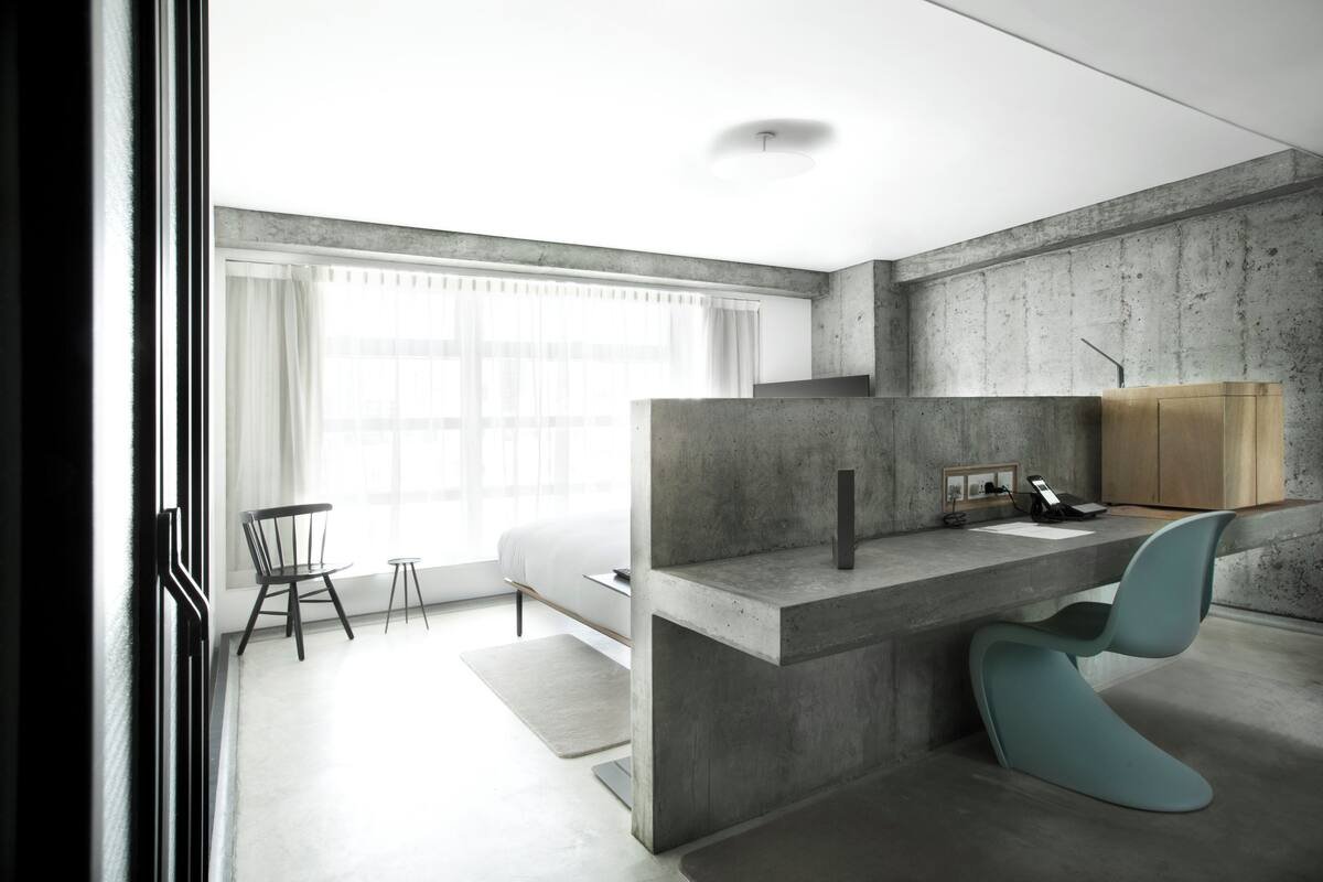 A modern kitchen with a concrete countertop, a wooden cabinet, and a blue chair.