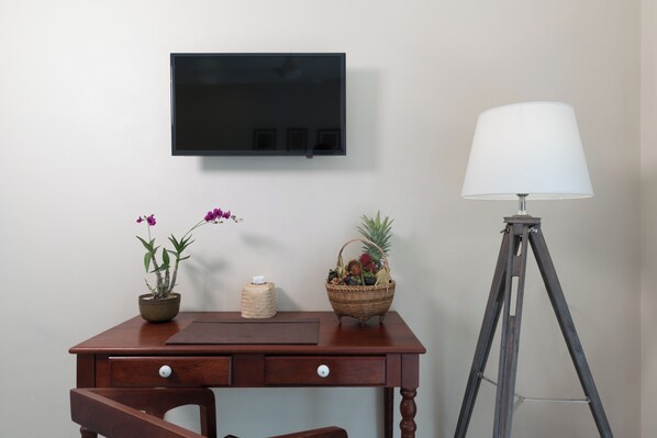 A wooden desk with a television mounted above it, a lamp, and two potted plants.