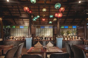 A restaurant interior with wooden ceilings, hanging lanterns, and a variety of tableware displayed on shelves. - Maison Dalabua (Luang Prabang)