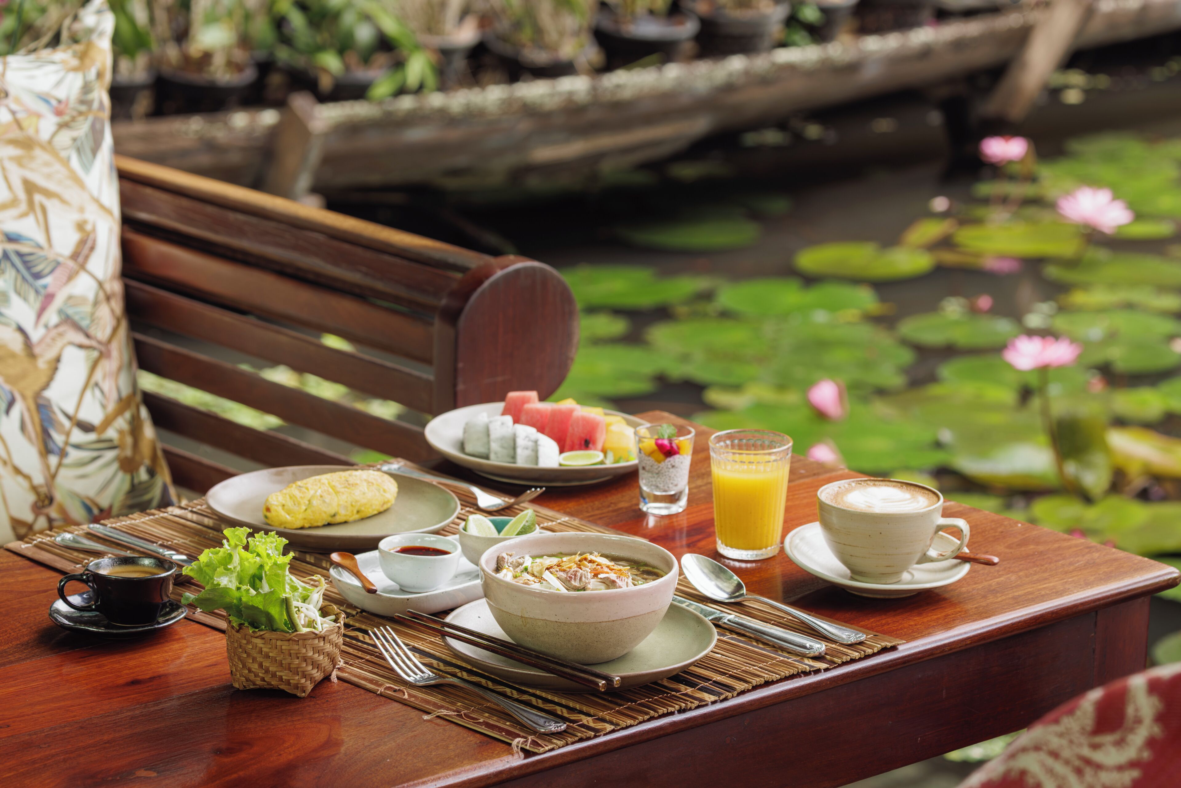 A wooden table with a meal setup including a bowl of soup, a plate of food, a cup of coffee, and a glass of orange juice.