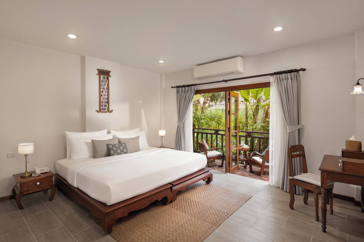 Habitación de hotel con una cama grande, una mesita, una silla y un balcón con vistas a zonas verdes.