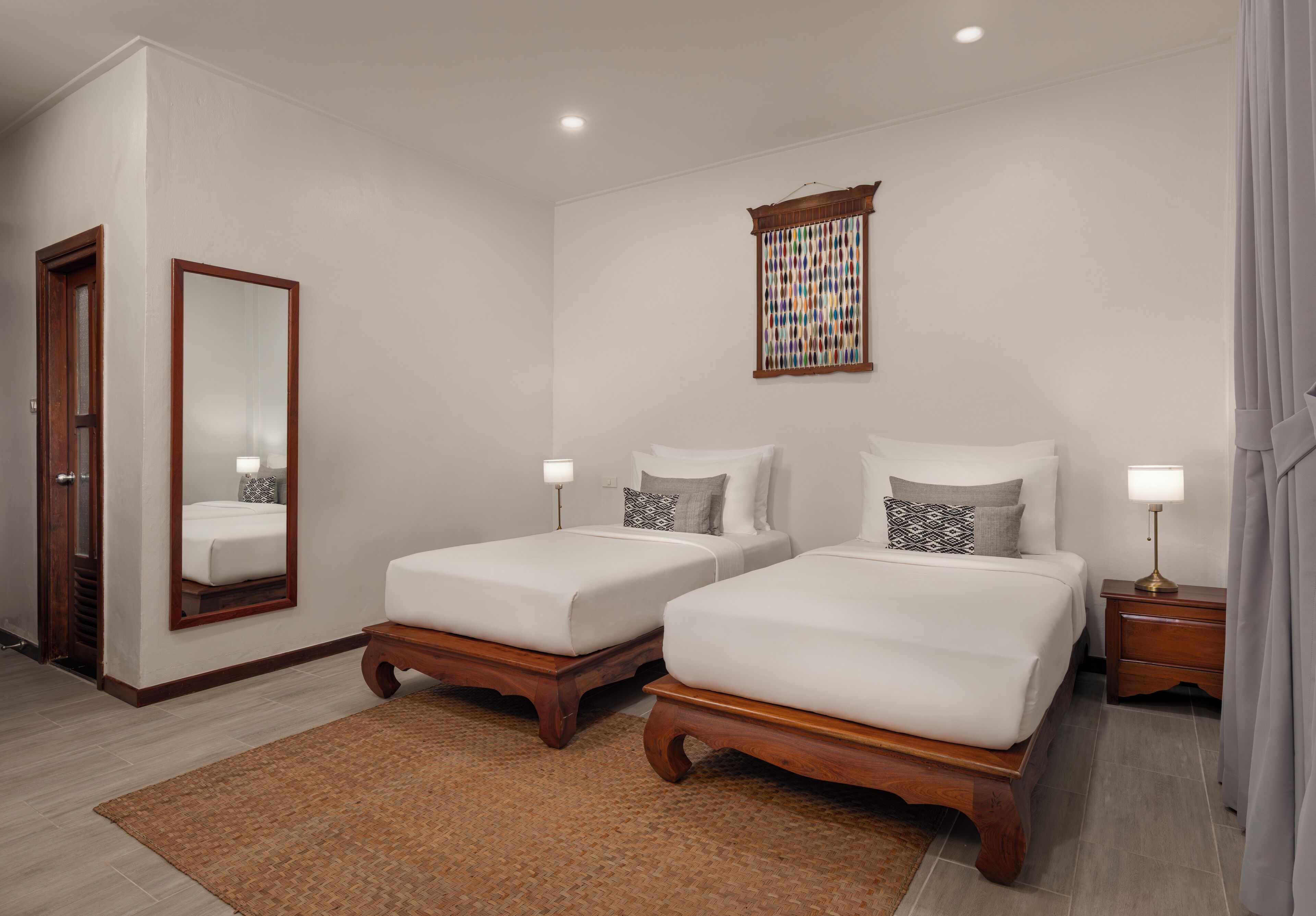Habitación de hotel con dos camas, un espejo grande, una obra de arte en la pared y una mesita de noche pequeña con una lámpara.