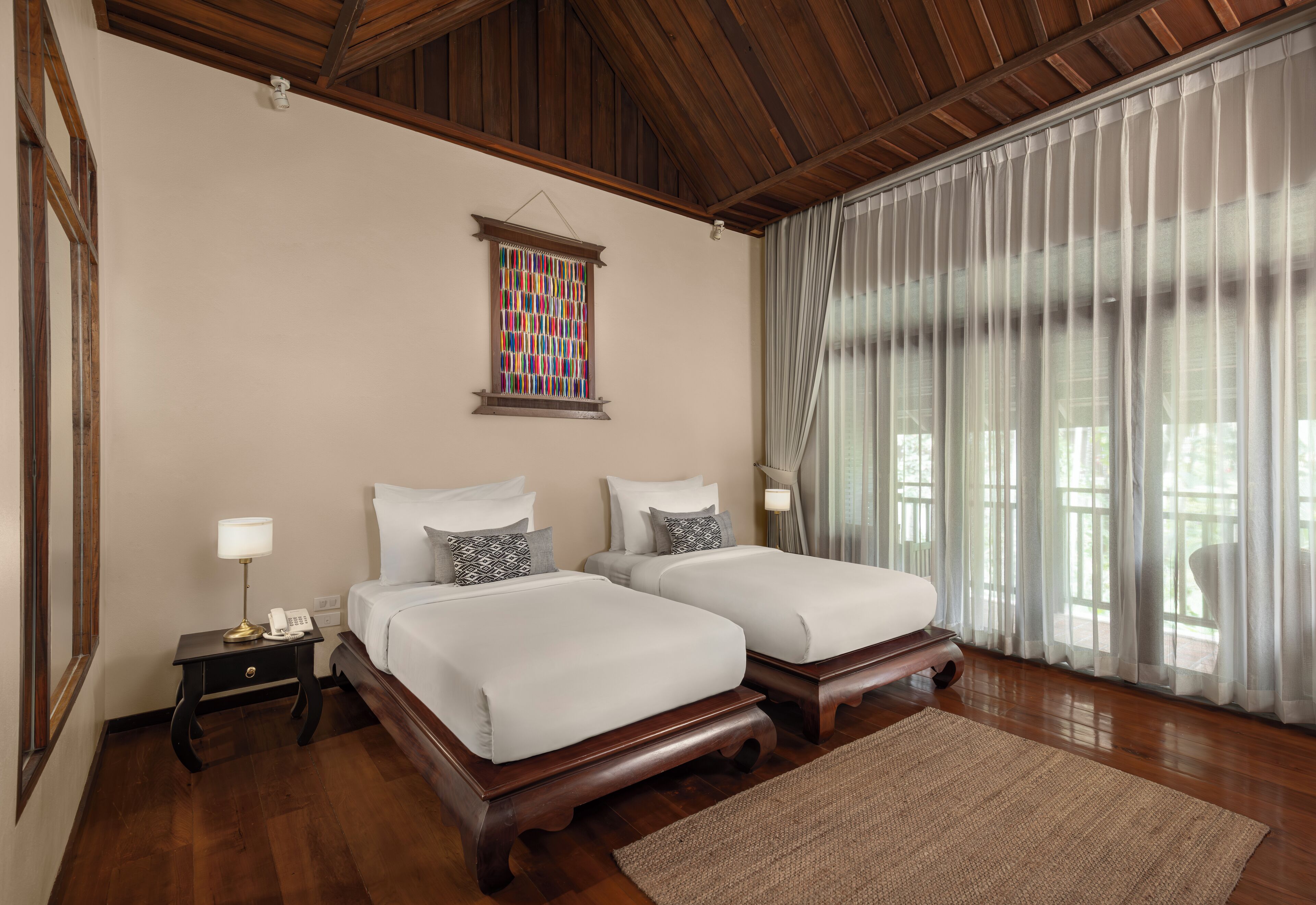 Habitación de hotel con dos camas, techo de madera, ventanal de vitral y un ventanal grande con cortinas.