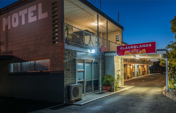 Un motel con balcón, un letrero que dice 'CLAUDELANDS MOTEL' y un camino de entrada pavimentado.