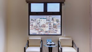 A room with two chairs and a small table with water bottles, a window with a city view, and a ceiling fan. - Boss Palace Hotel (Ho Chi Minh City)