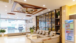 A modern hotel lobby with a large sectional sofa, a coffee table, and a refrigerator stocked with beverages. - Boss Palace Hotel (Ho Chi Minh City)