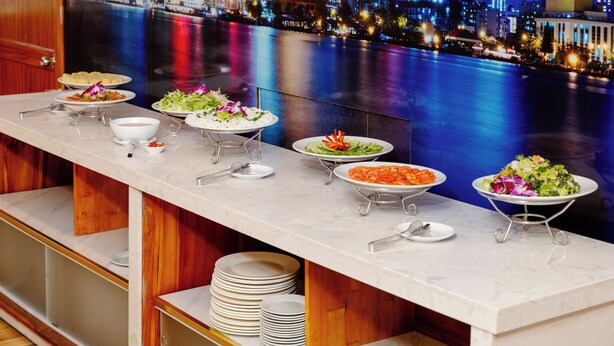 A buffet setup with various dishes, a cityscape view, and a marble countertop. - Boss Palace Hotel (Ho Chi Minh City)