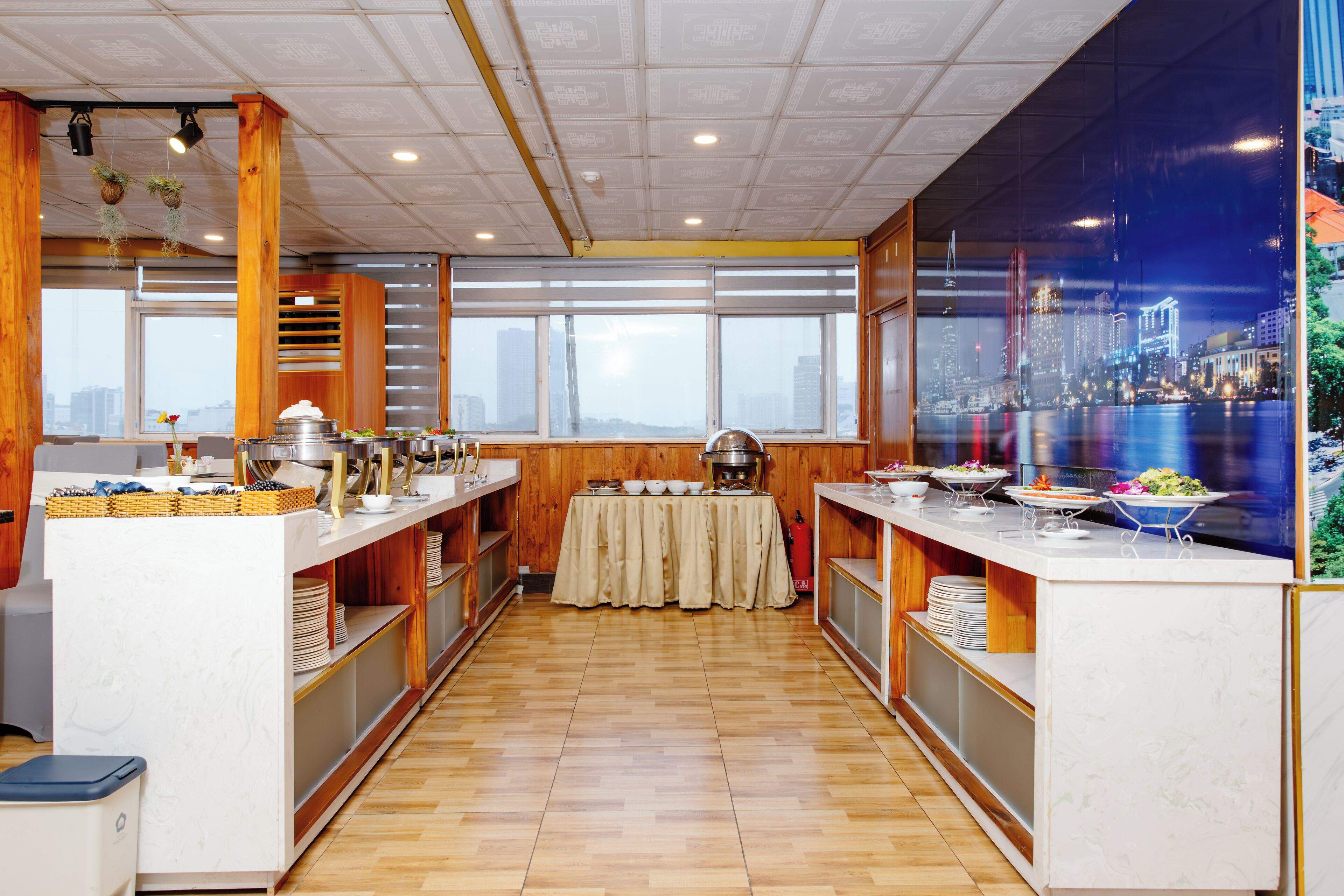 A spacious kitchen with wooden cabinets, a central island with a table, and a cityscape view through a large window.