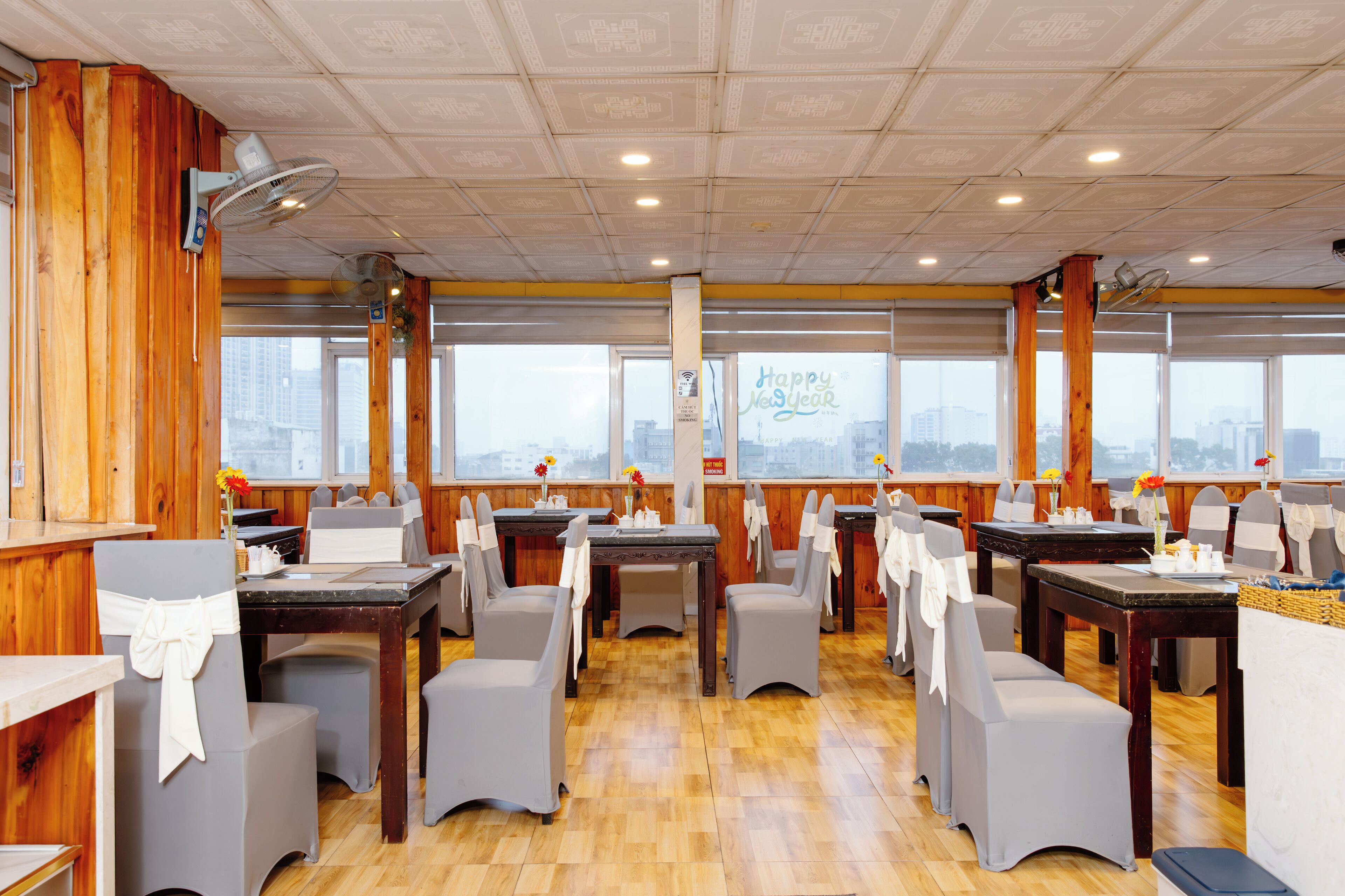 A restaurant with wooden walls, multiple tables and chairs, and large windows with a city view.