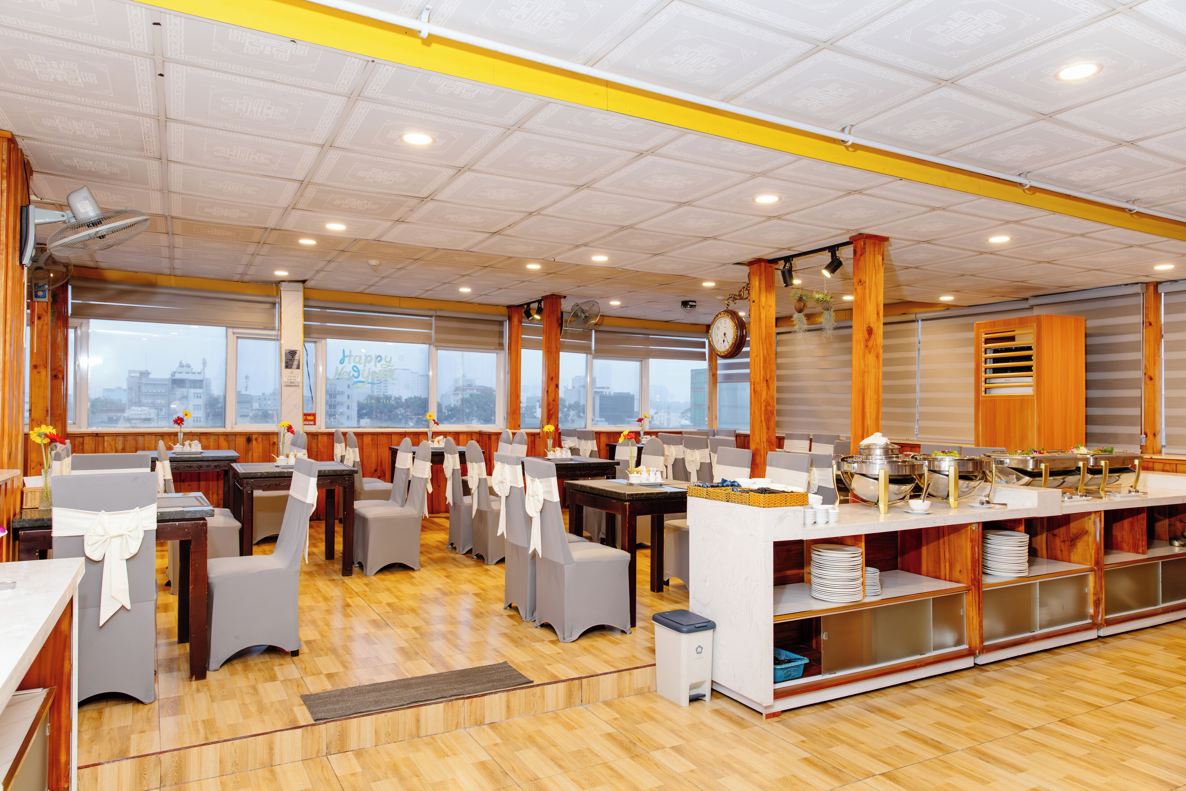 A restaurant with multiple tables and chairs, a buffet setup, and large windows.