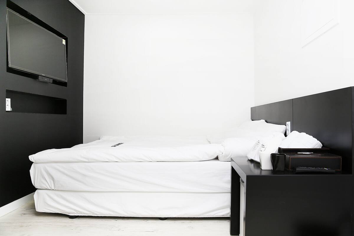 A minimalist hotel room with a bed, bedside table, and a TV mounted on the wall.